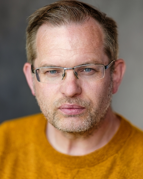 Phil Gwilliam wearing glasses and a mustard jumper